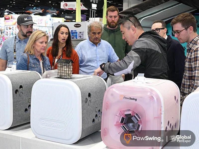 Pet industry buyers gather around white, gray and pink PawSwing cat self-grooming houses at the PawSwing booth at Global Pet Expo 2026